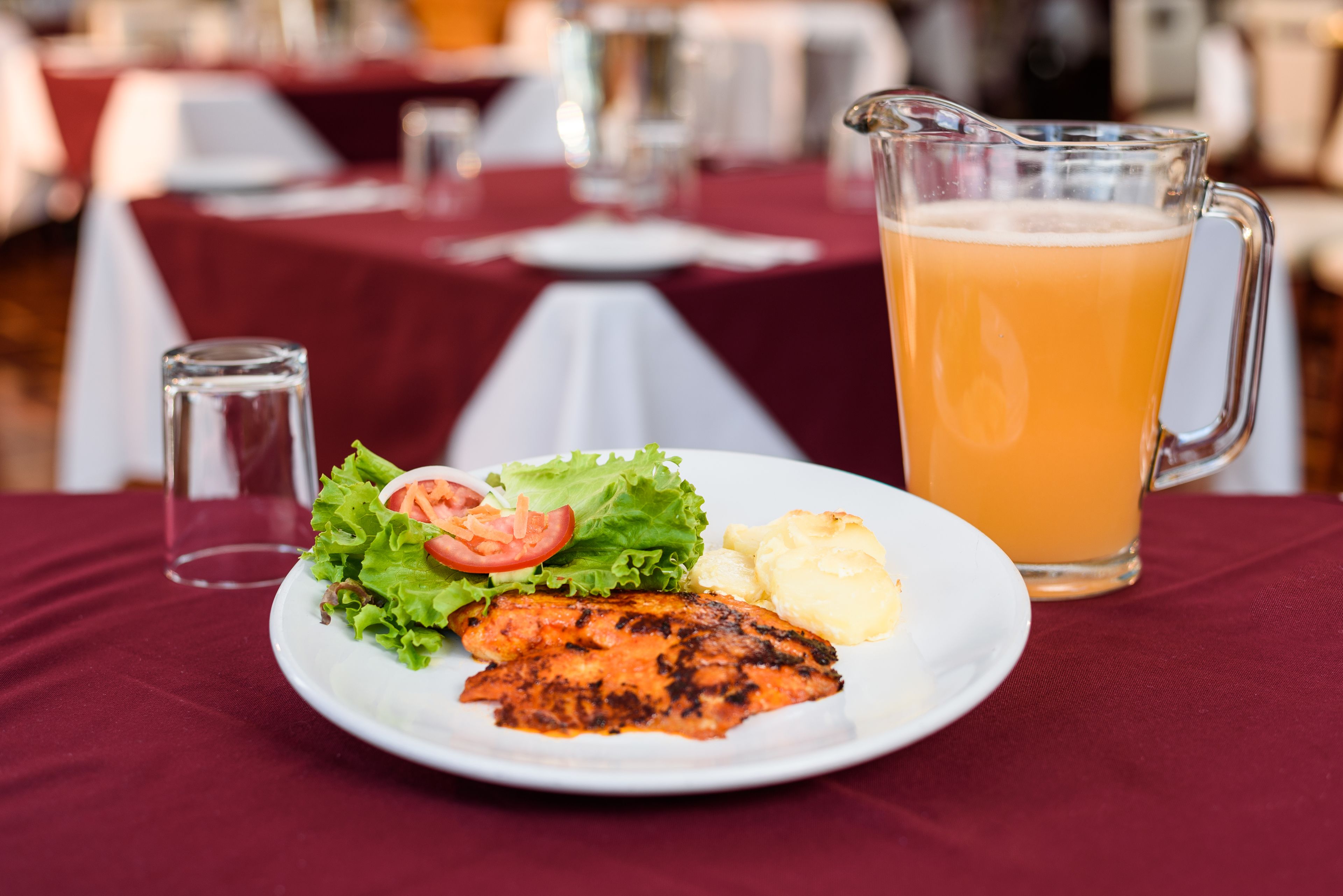 A plate with grilled fish, salad, and potatoes, and a pitcher of orange juice on a table.