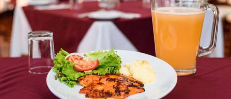 A plate with grilled fish, salad, and potatoes, and a pitcher of orange juice on a table.
