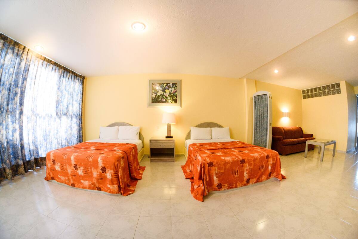 Ein Hotelzimmer mit zwei Betten, einem Schlafsofa, einem Nachttisch und einer Lampe.