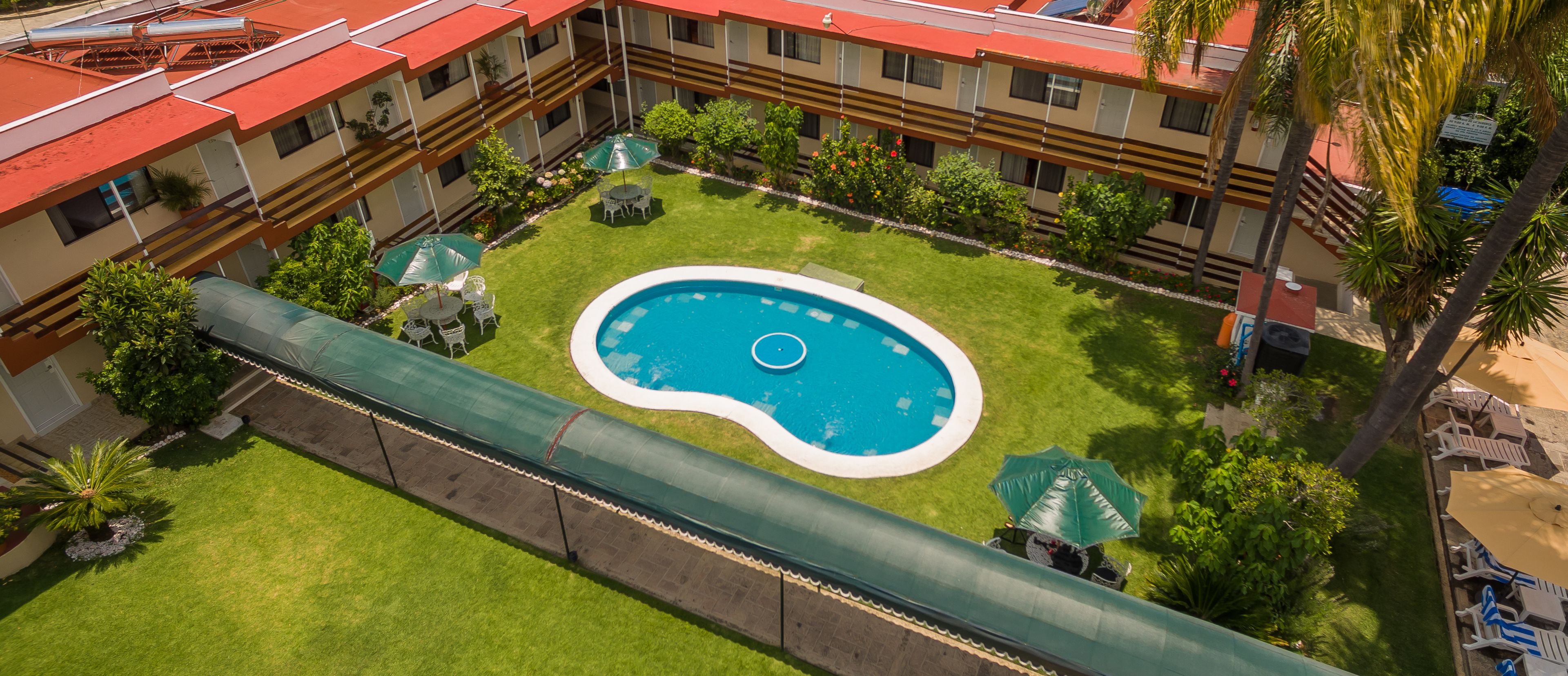 A hotel courtyard with a swimming pool, outdoor seating, and palm trees.