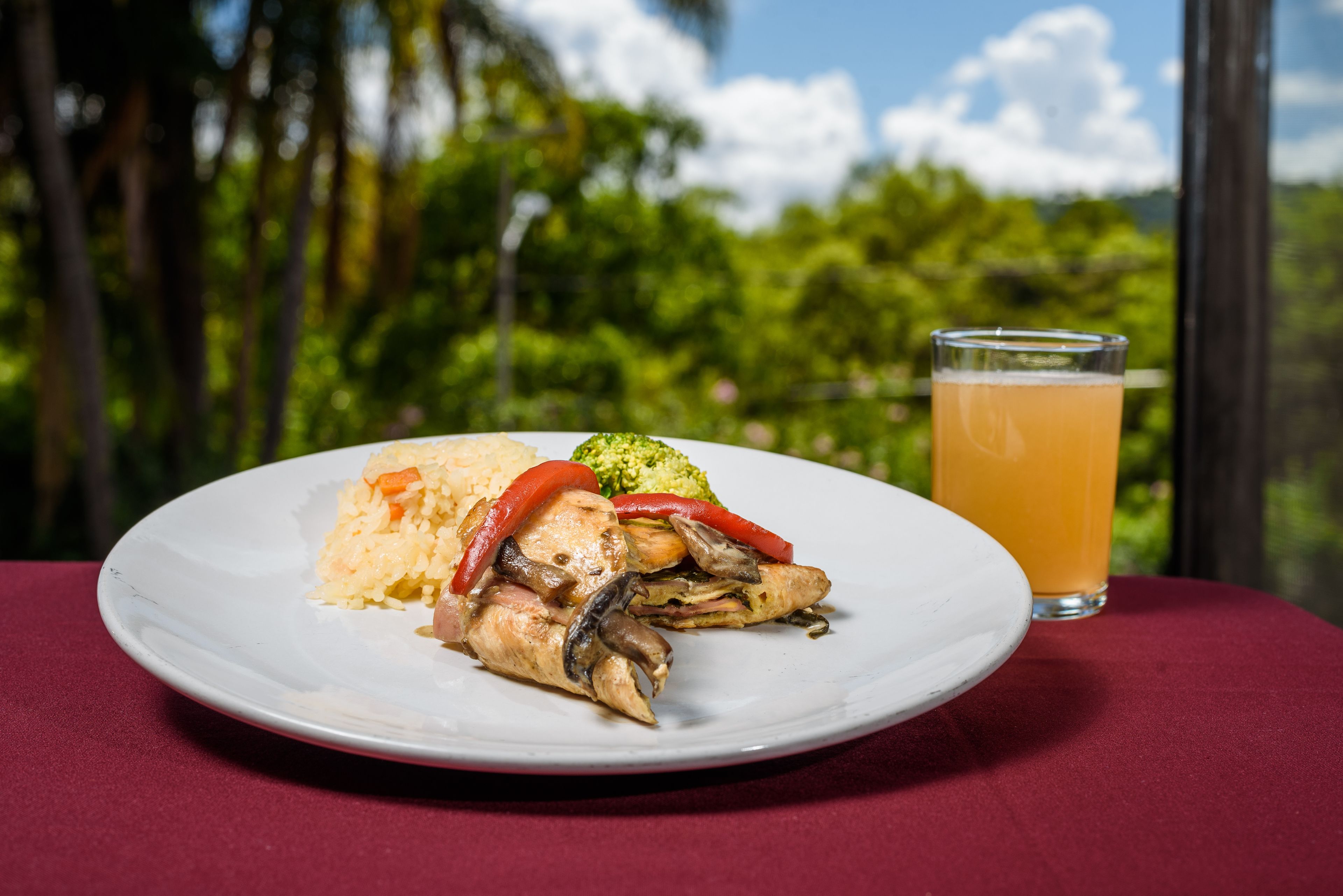 Un plato de comida con arroz, verduras y pollo, junto a un vaso de jugo de naranja sobre una mesa con mantel rojo.