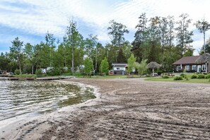 Une propriété au bord du lac, dotée d’une plage de sable, d’une jetée en bois et d’une maison au toit de chaume.