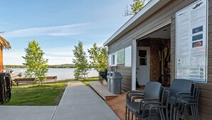 A lakeside cabin with outdoor seating, a map, and a signboard. - Les Chalets Baie Cascouia (Larouche)