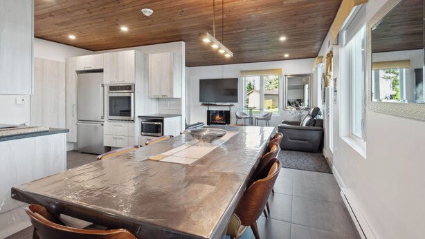 A modern kitchen with a large island, built-in appliances, and a dining area with a long table and chairs. - Les Chalets Baie Cascouia (Larouche)