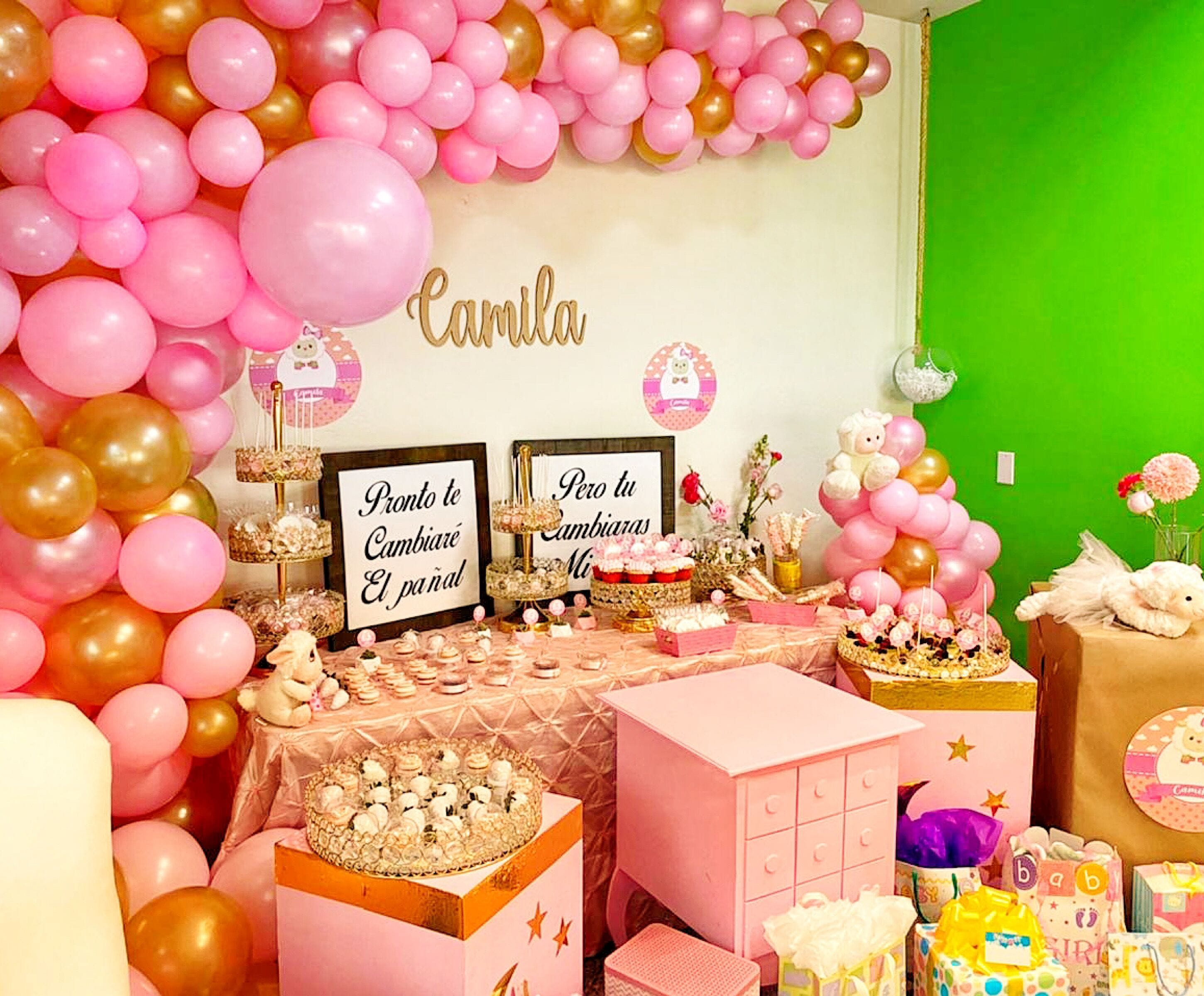 Un espace événementiel décoré de ballons roses et dorés, une table garnie de desserts et un fond vert en arrière-plan.