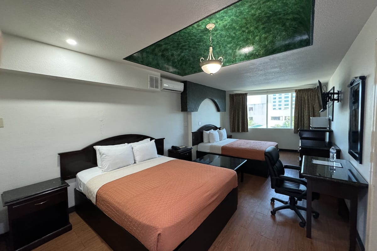 Habitación de hotel con dos camas, un escritorio, una silla, una lámpara de escritorio e iluminación en el techo.