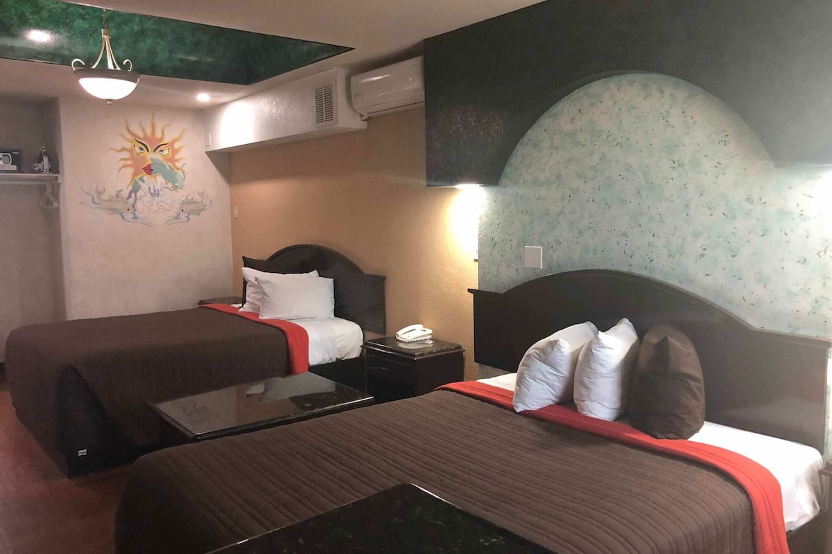 Habitación de hotel con dos camas, un escritorio, un teléfono y un mural en la pared.