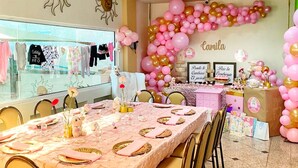 A dining area with a long table set for a meal, chairs, and a wall decorated with balloons and a name sign.