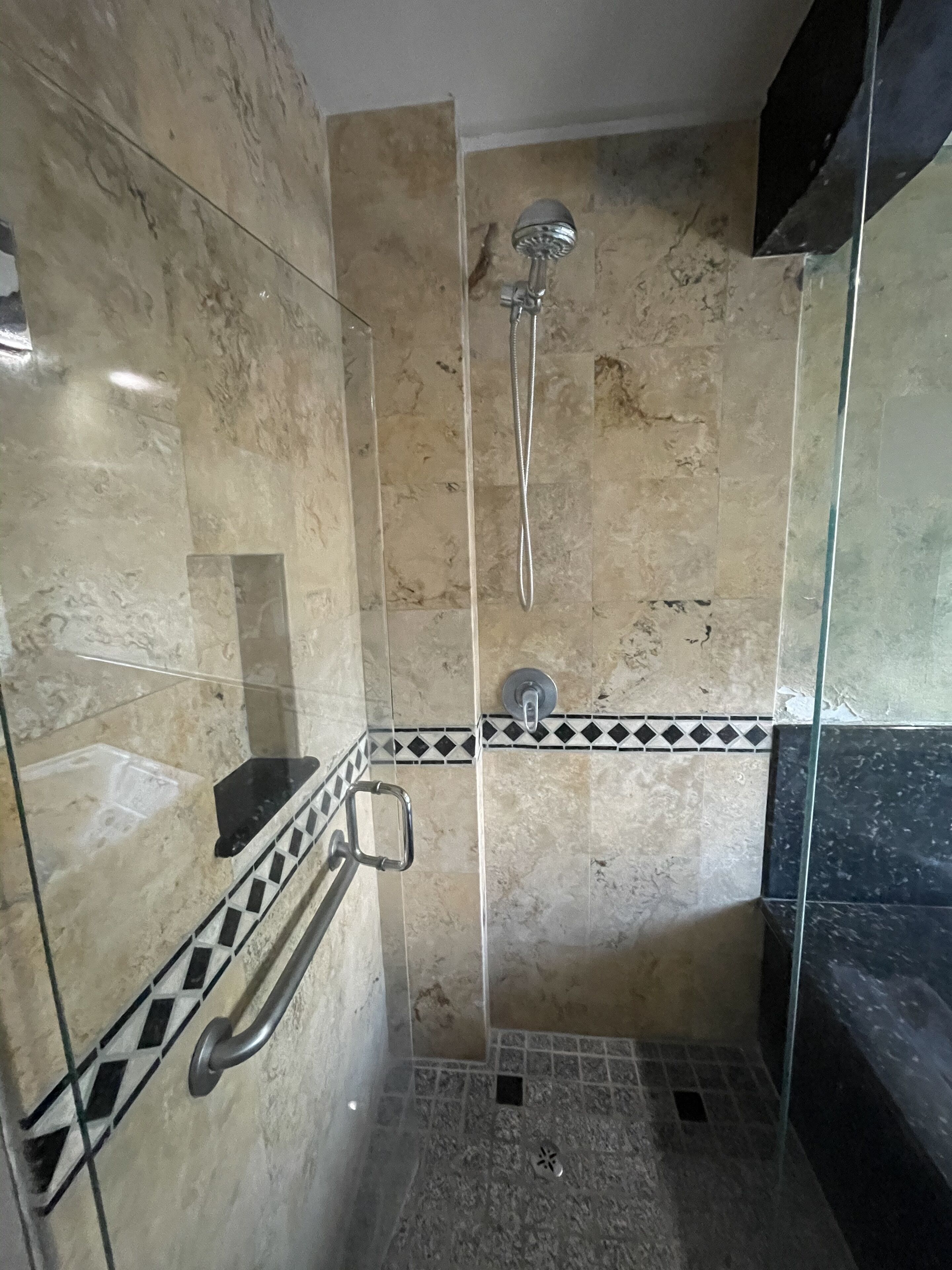 A glass-enclosed shower stall with a handheld showerhead and a wall-mounted faucet.