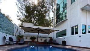 Una piscina con borde de baldosas, rodeada de plantas en macetas y mobiliario de exterior.