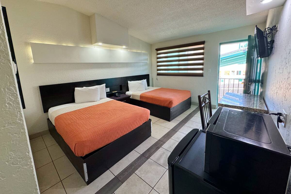 Una habitación de hotel con dos camas, un pequeño rincón americano y una ventana con persianas.