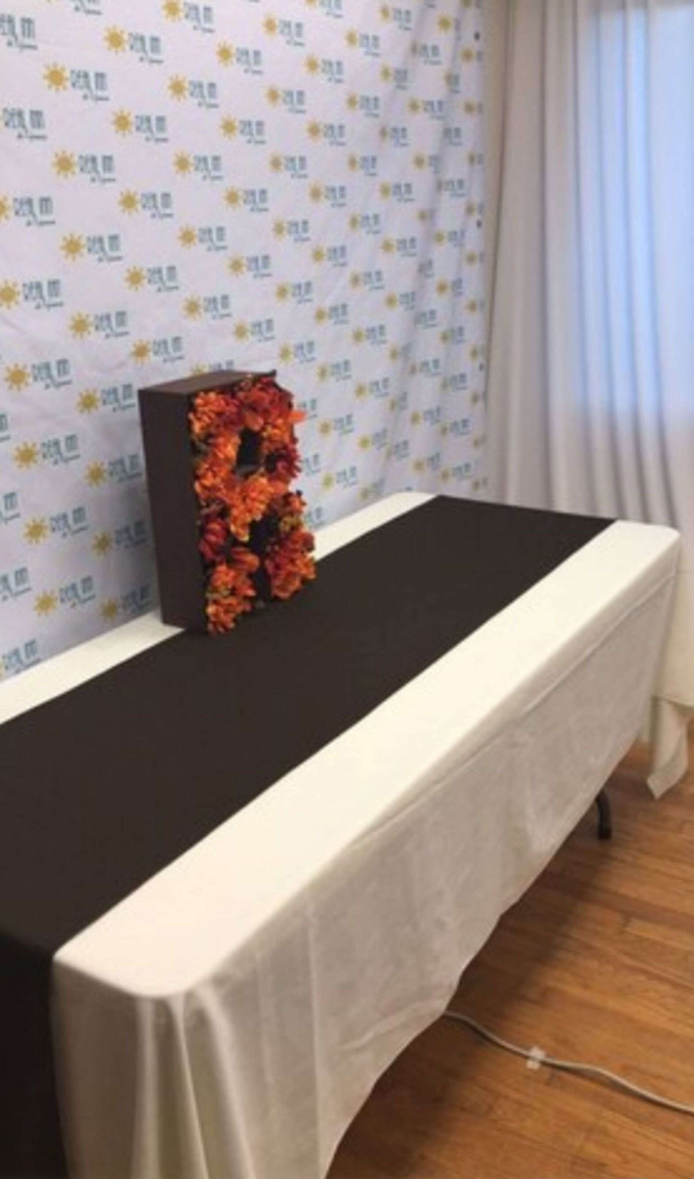 A table with a black top and white tablecloth, set against a patterned backdrop.