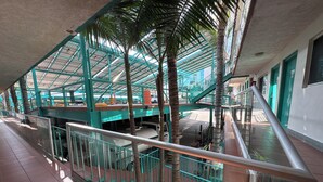 Un espacio interior de varios niveles con barandilla de cristal, palmeras y una escalera.