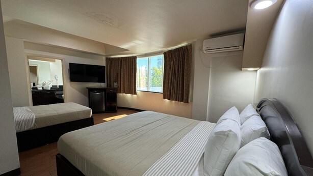 Habitación de hotel con dos camas, un televisor de pantalla plana, un equipo de aire acondicionado y una ventana con cortinas.