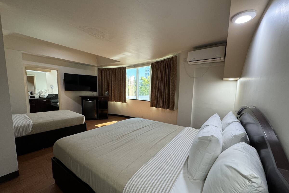 Habitación de hotel con dos camas, un televisor de pantalla plana, un equipo de aire acondicionado y una ventana con cortinas.