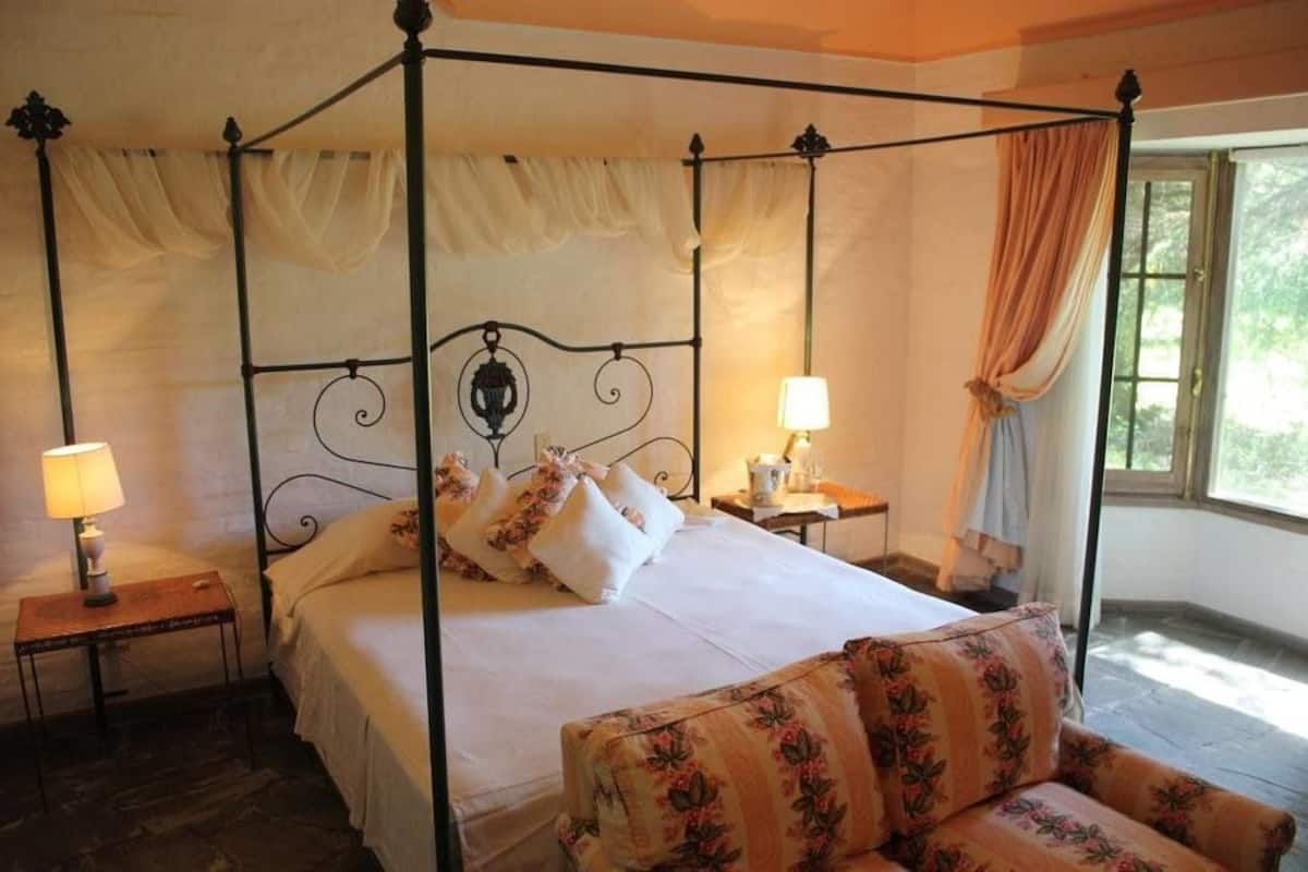 Una cama con dosel adornada con almohadillas estampadas, dos lámparas de noche y un sofá de motivos florales.