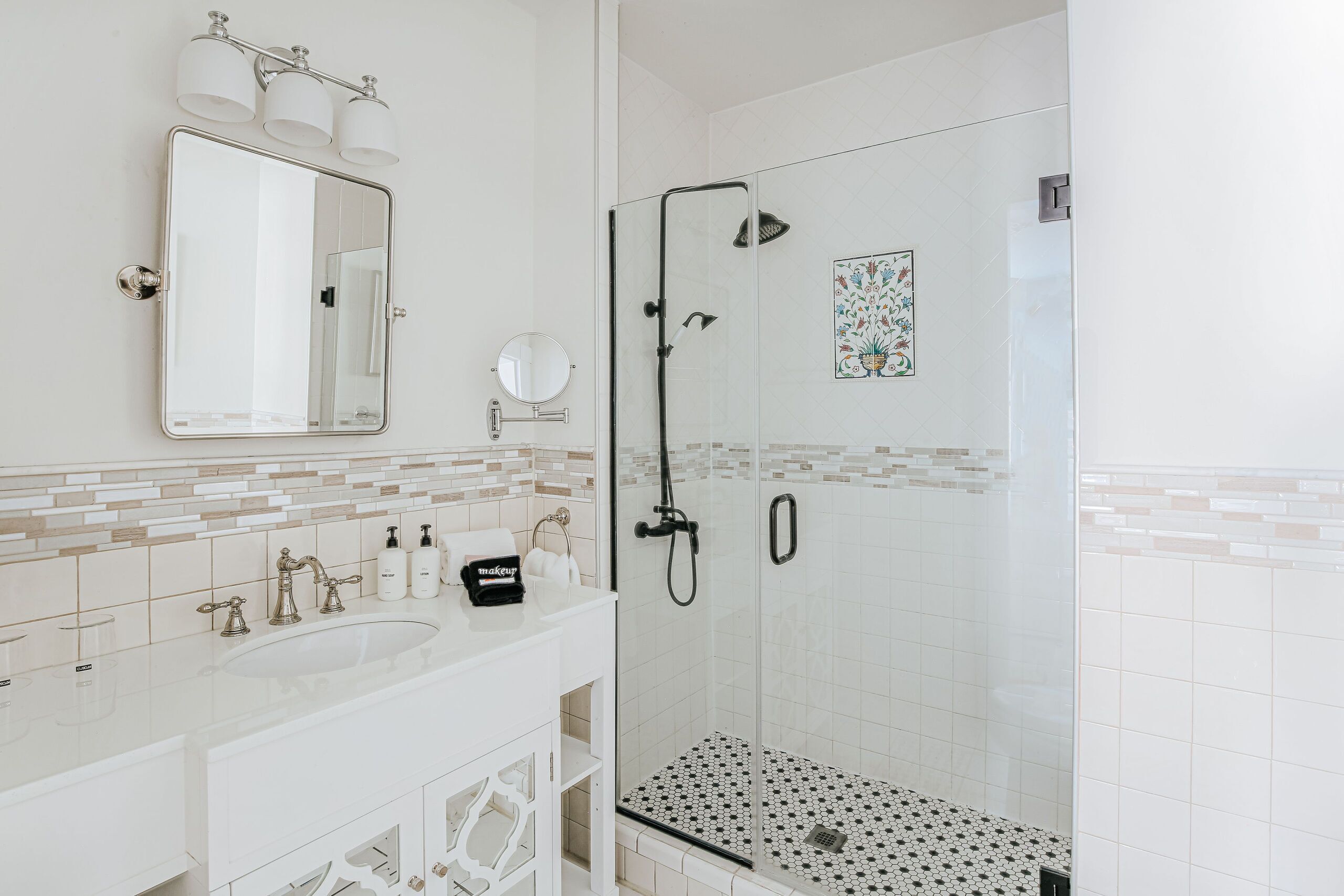 A modern bathroom with a glass-enclosed shower, a large mirror, and a white vanity with a sink and two faucets.
