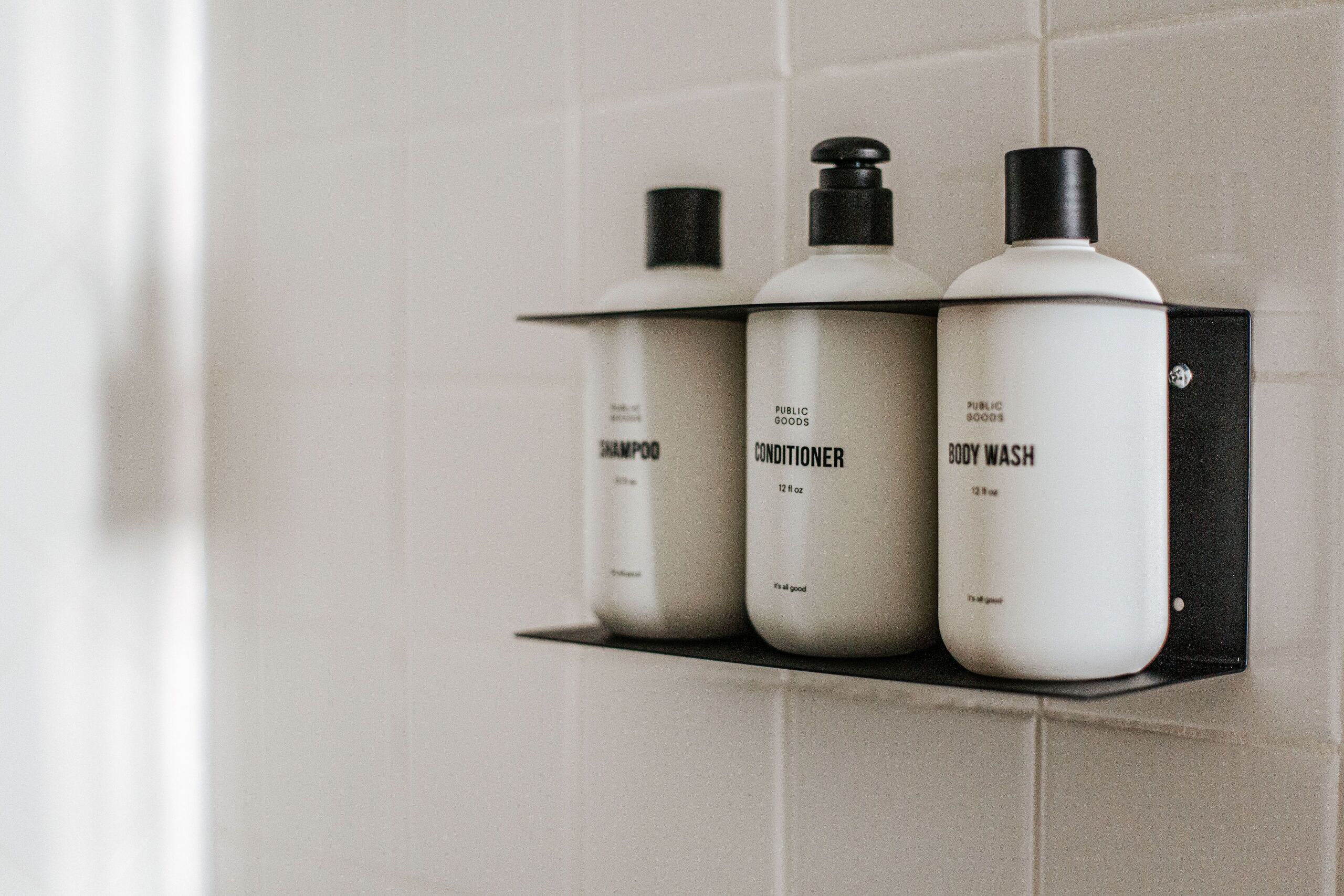 Three bottles of toiletries on a shelf against a tiled wall.