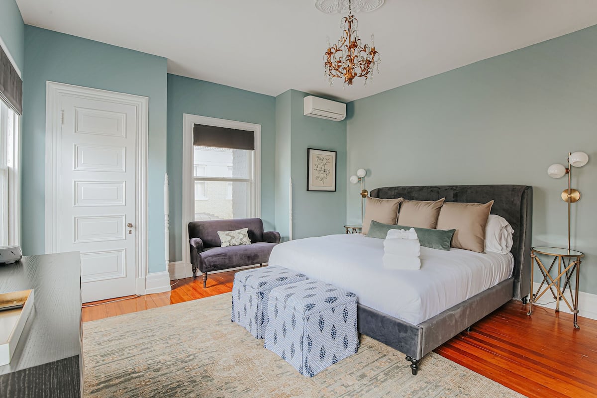 A bedroom with a large bed, a chair, a chandelier, and a floor lamp.