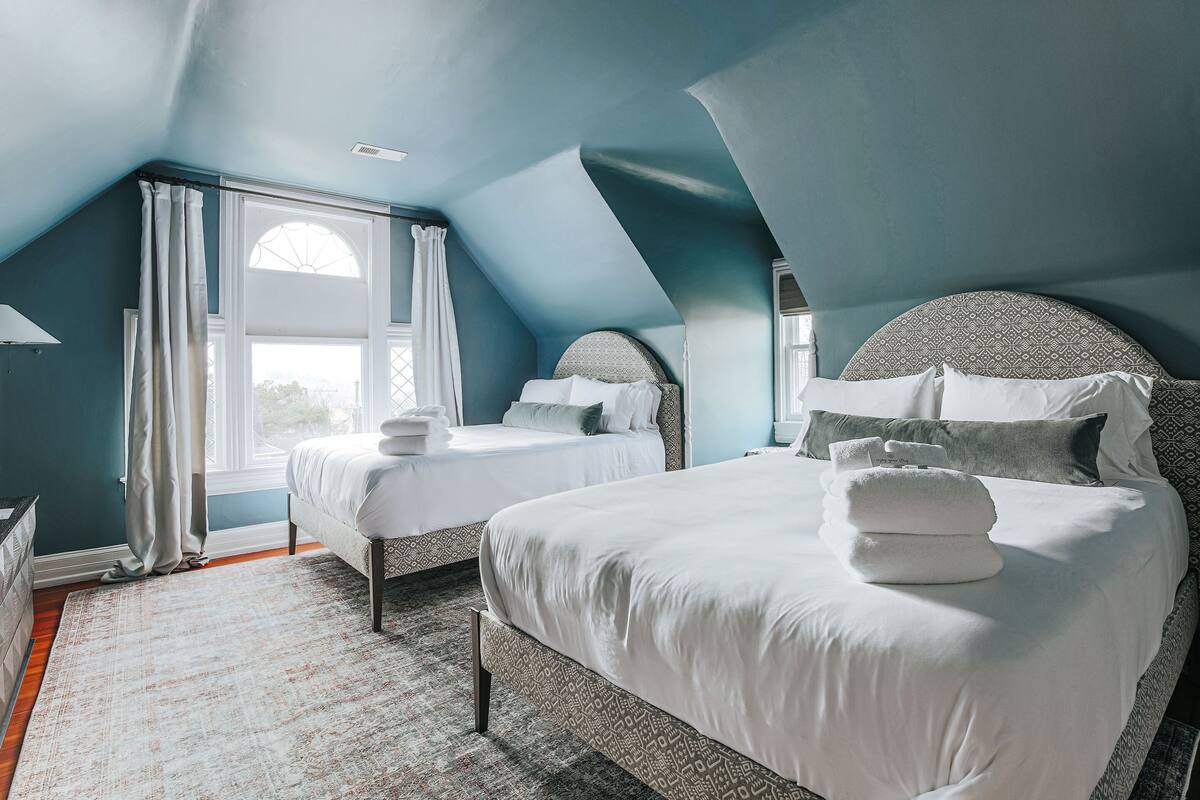 A bedroom with two beds, a large window, and a patterned rug.