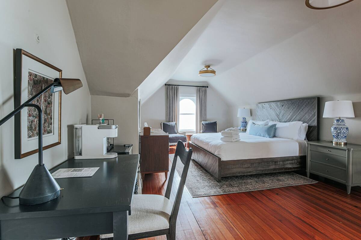 A bedroom with a bed, bedside tables, a desk with a chair, a lamp, and a window with curtains.