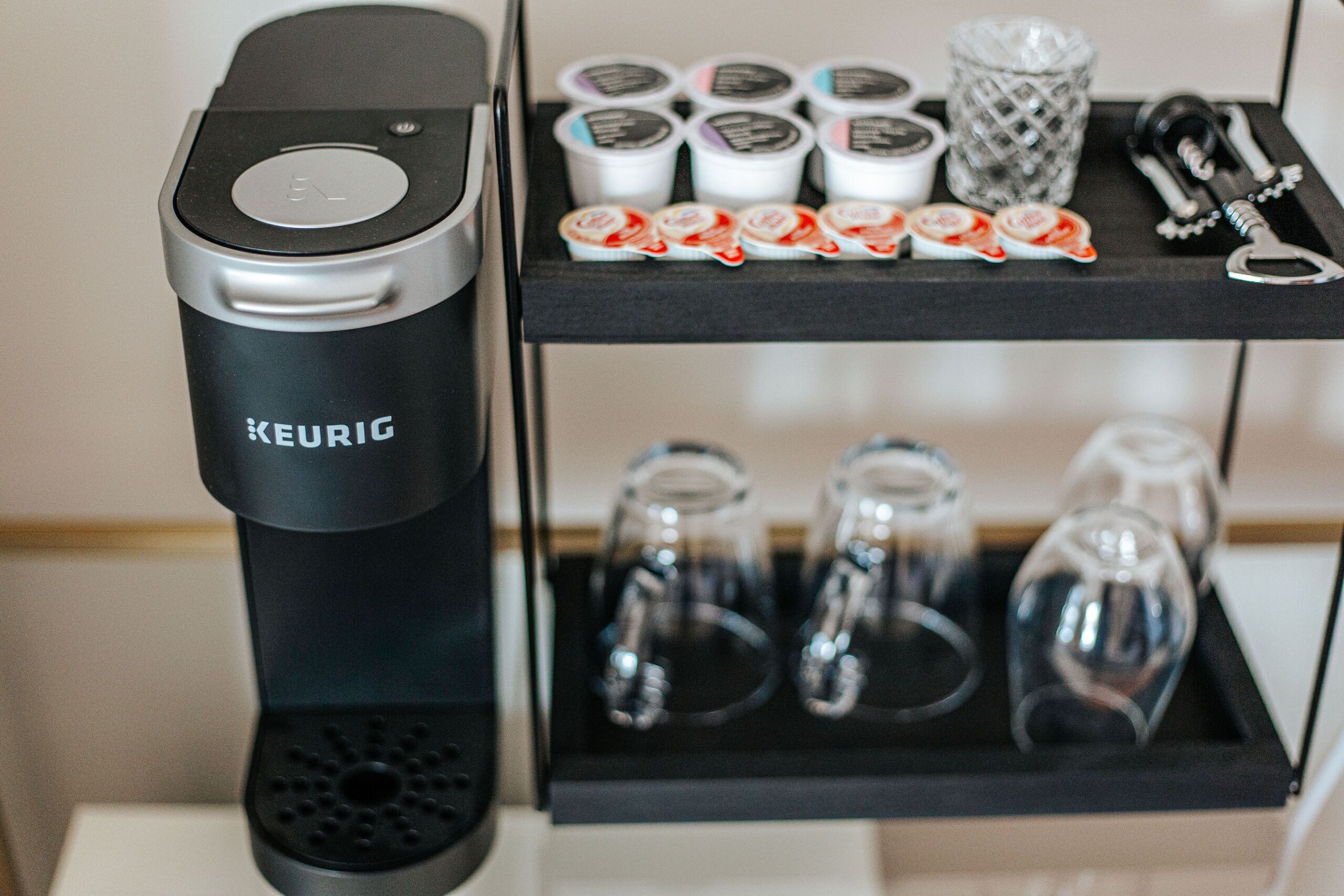 A KEURIG coffee maker on a black tray with a glass carafe, a coffee grinder, and a coffee pod holder.