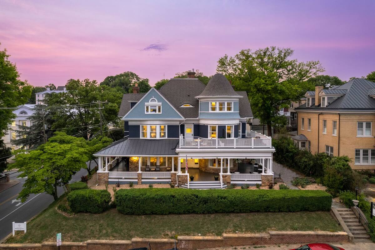 A large two-story house with a wrap-around porch, multiple windows, and a chimney.