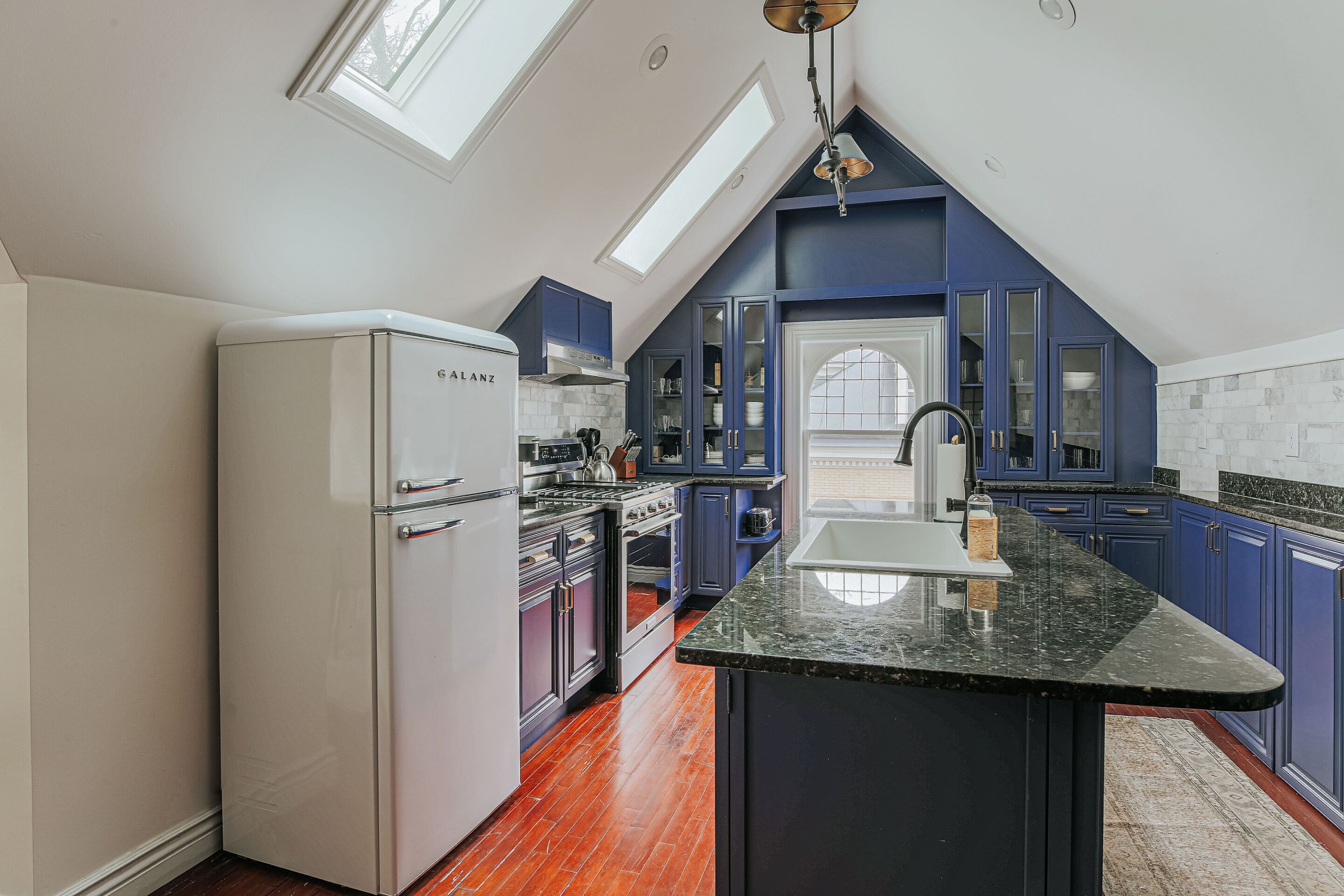 A modern kitchen with a white refrigerator, dark blue cabinets, a black granite countertop, and a skylight.