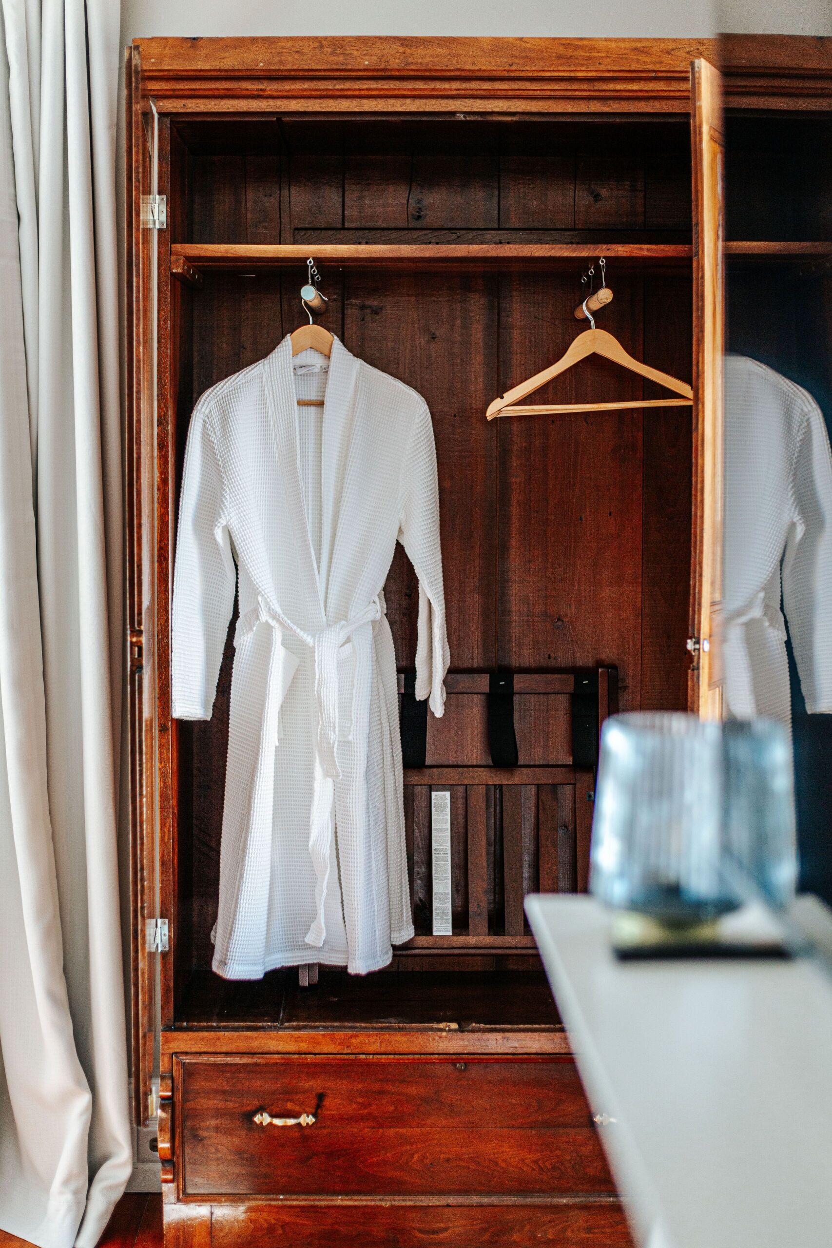 A wooden wardrobe with two white robes hanging inside.