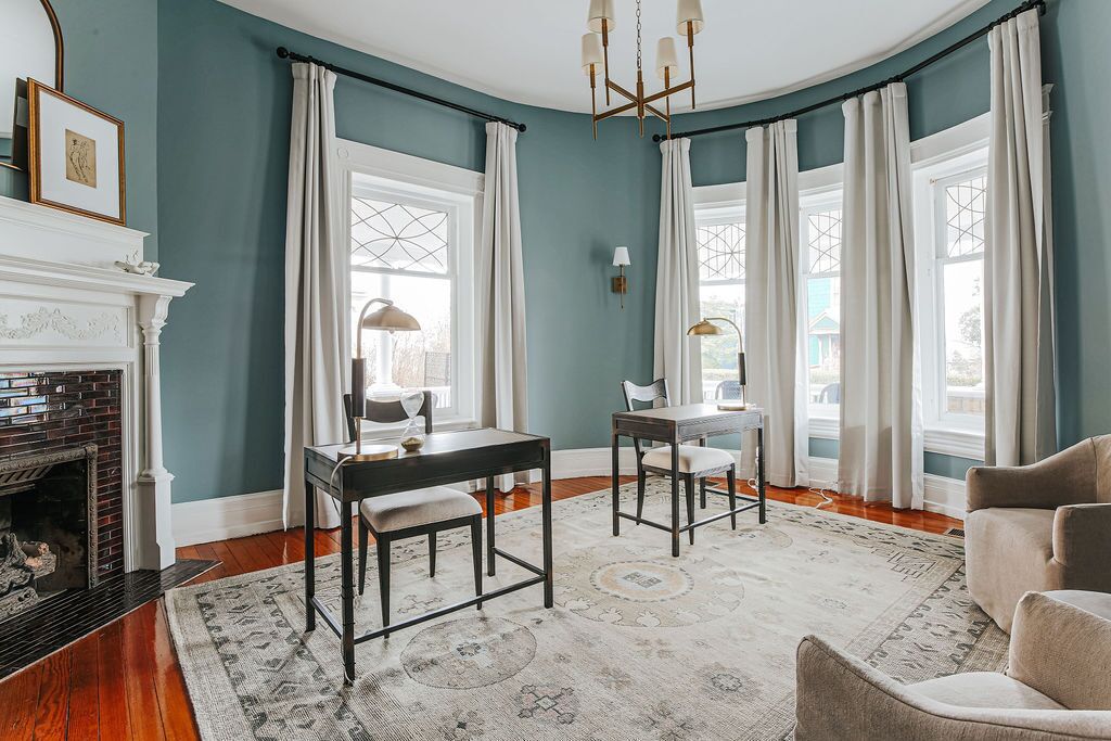 A room with a fireplace, a dining table with chairs, a chandelier, and large windows with curtains.