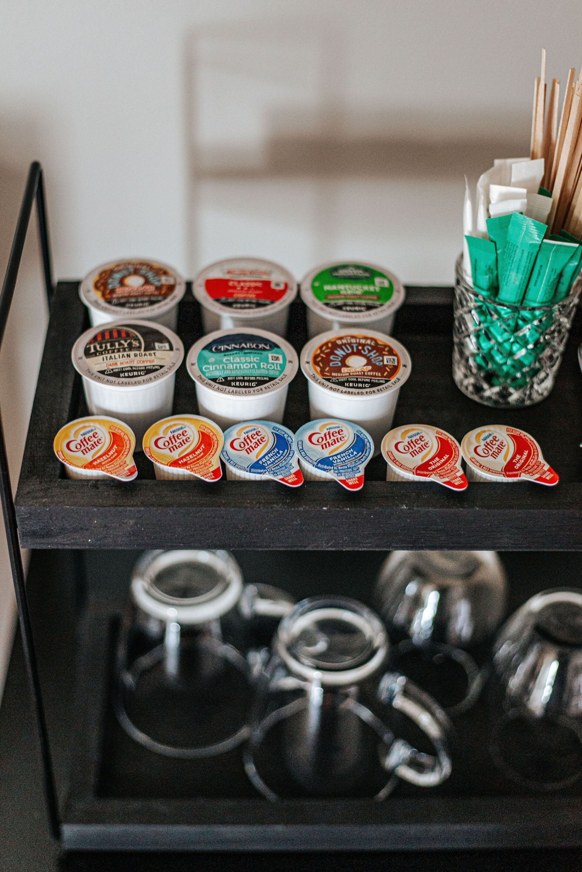 A coffee station with various coffee pods and a glass container with straws.