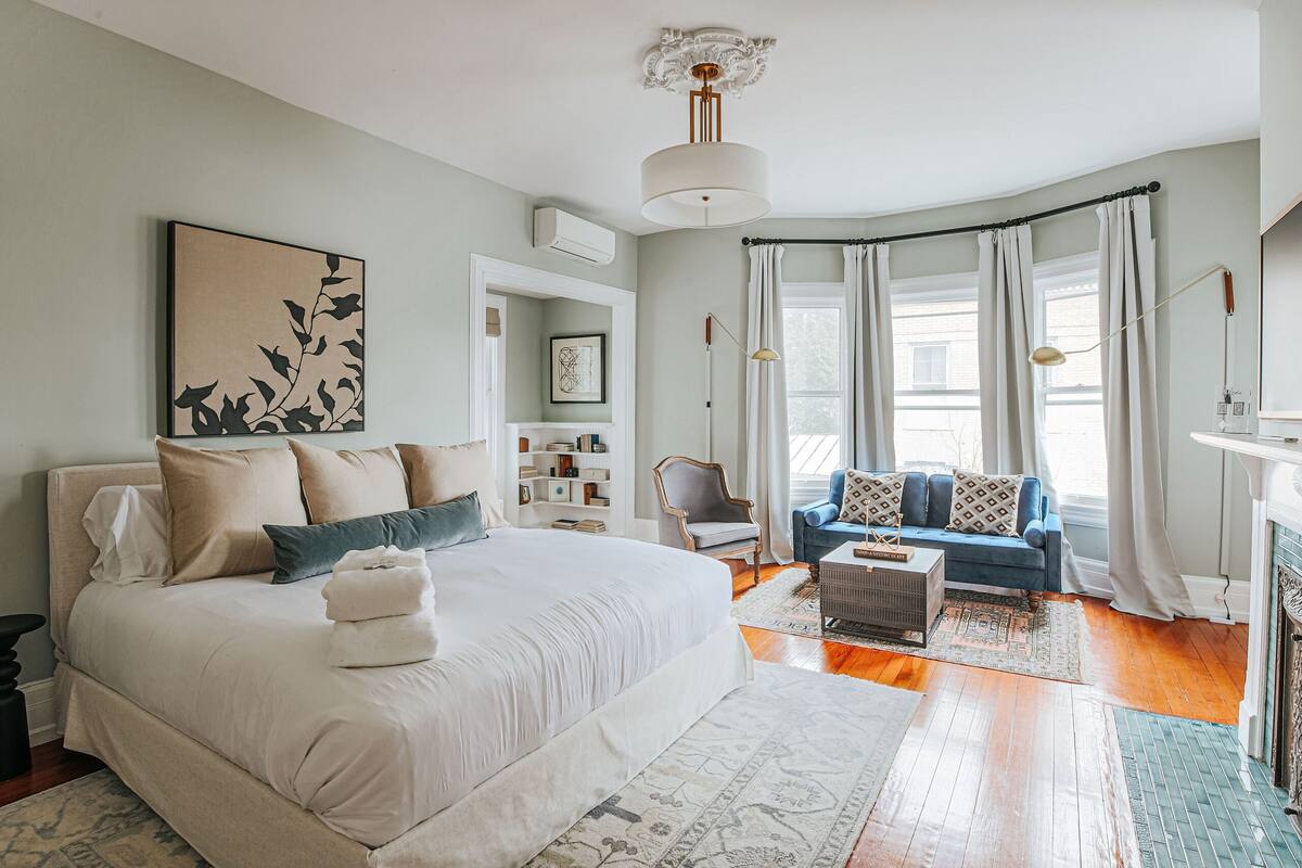 A bedroom with a large bed, a blue sofa, a fireplace, and a bookshelf.