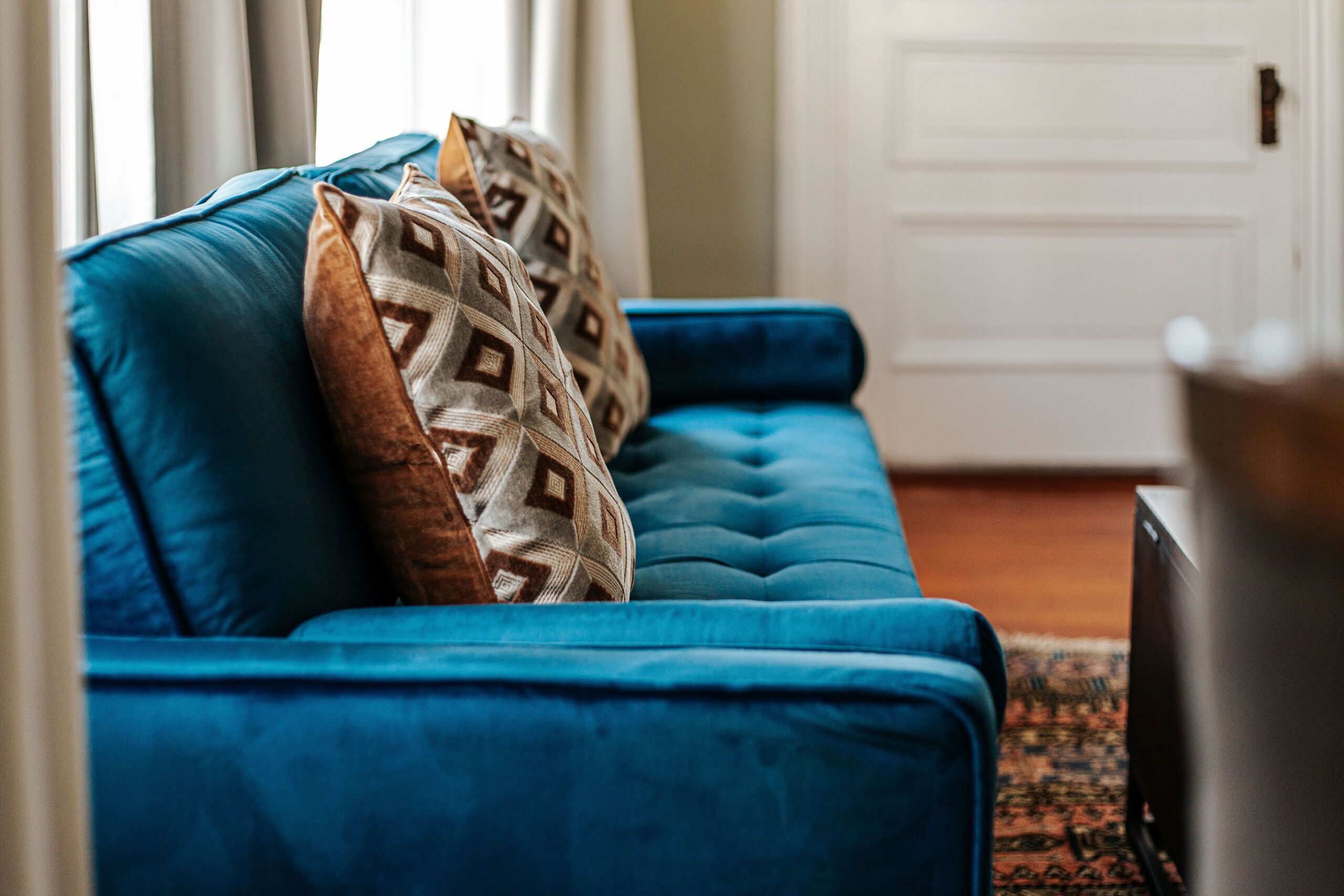 A blue sofa with patterned cushions in a room with a white door and a rug.