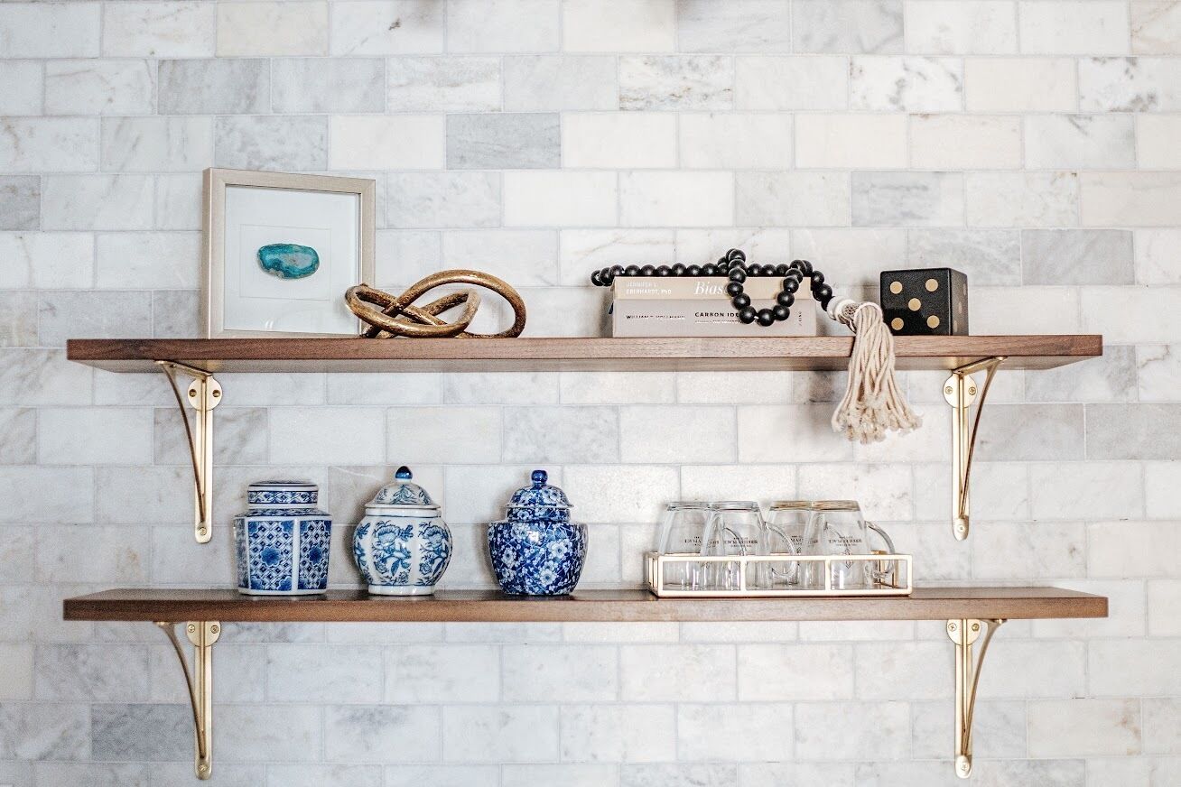 Une étagère en bois ornée d’objets décoratifs, le tout adossé à un mur recouvert de carreaux.
