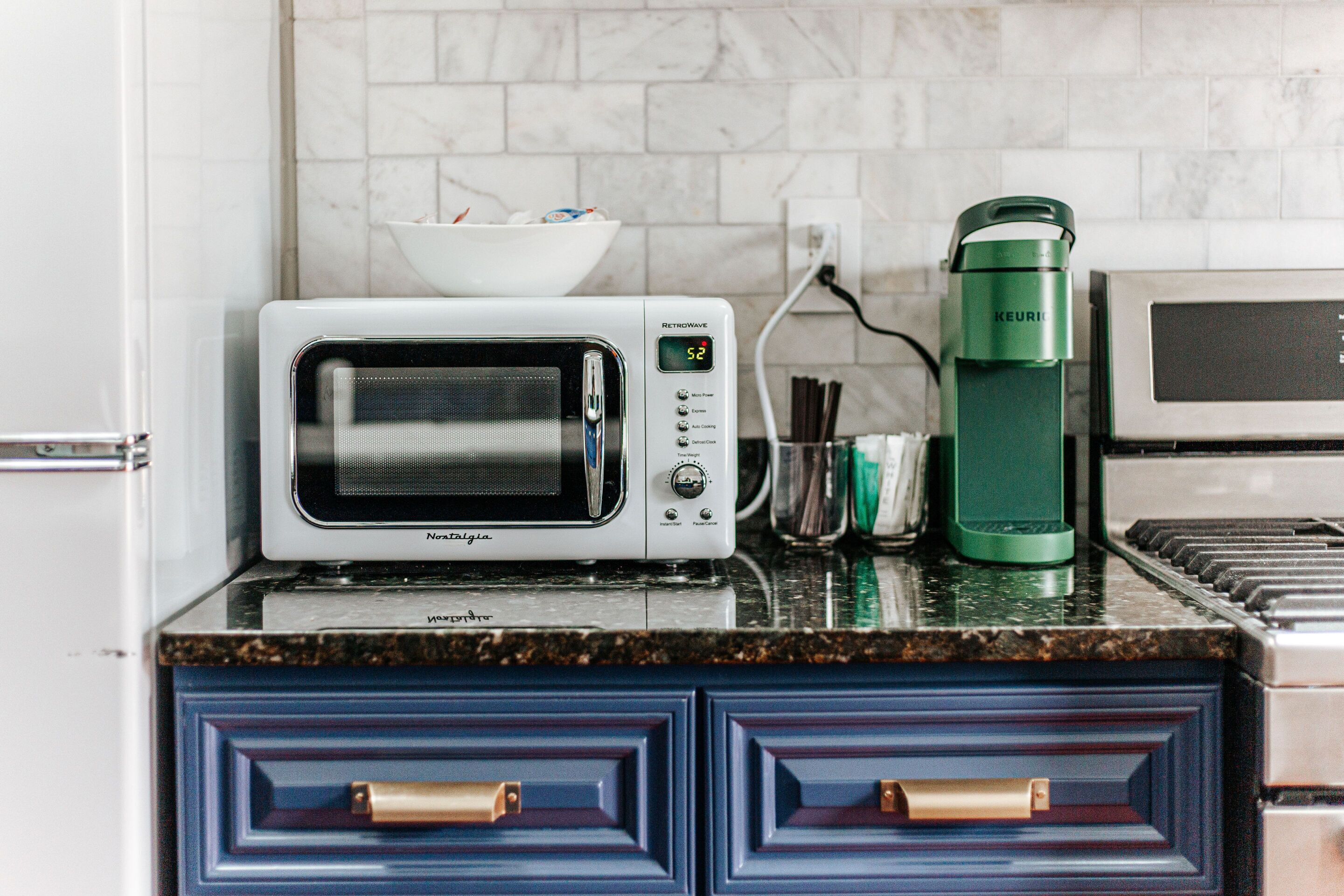 A kitchen with a white microwave, a green water dispenser, and a bowl of cereal on the counter.