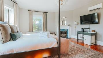 A bedroom with a large bed, a desk, a television, and a fireplace.