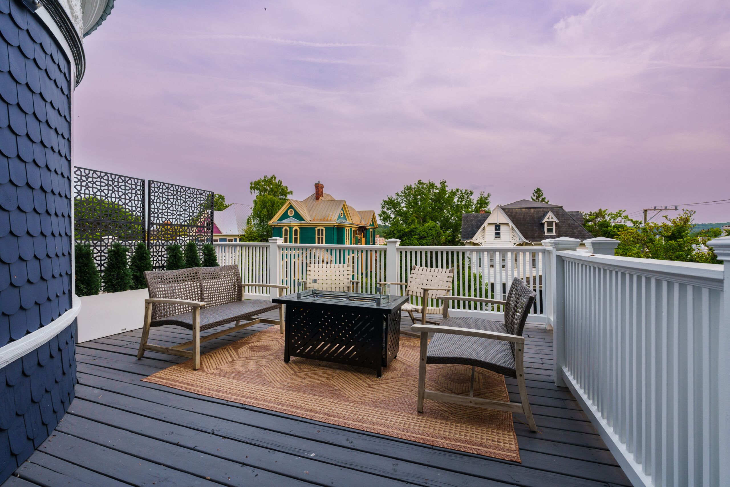 Una terraza con mesa y sillas, una cerca decorativa y vistas a casas al fondo.