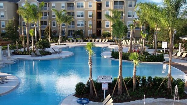 Área de piscina de hotel com várias espreguiçadeiras, palmeiras e uma placa de 'Não Mergulhar'.