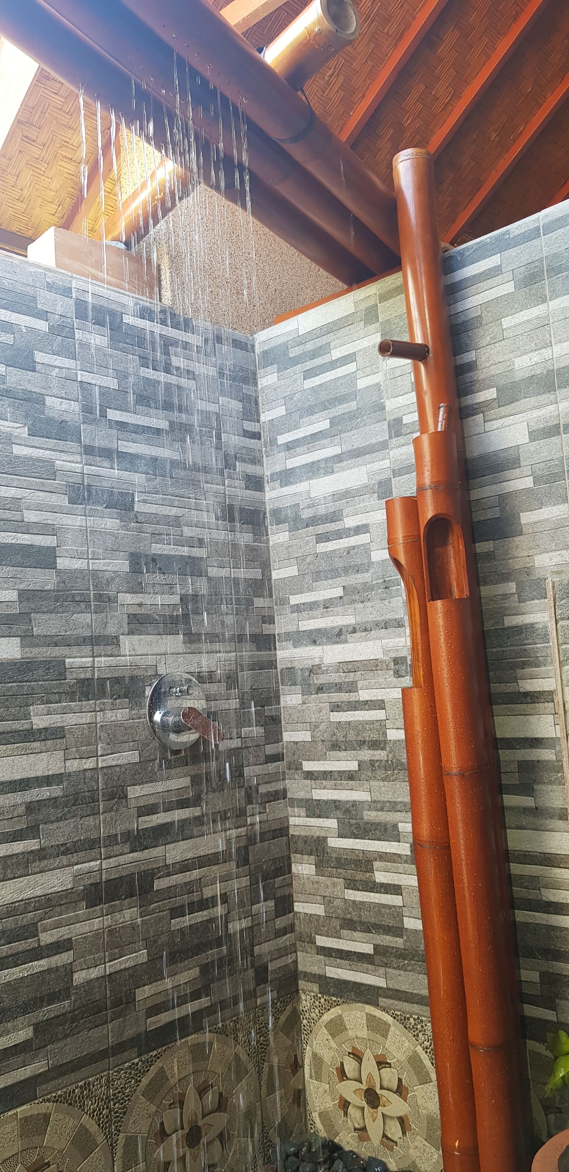 A shower with a stone wall and a wooden ceiling.