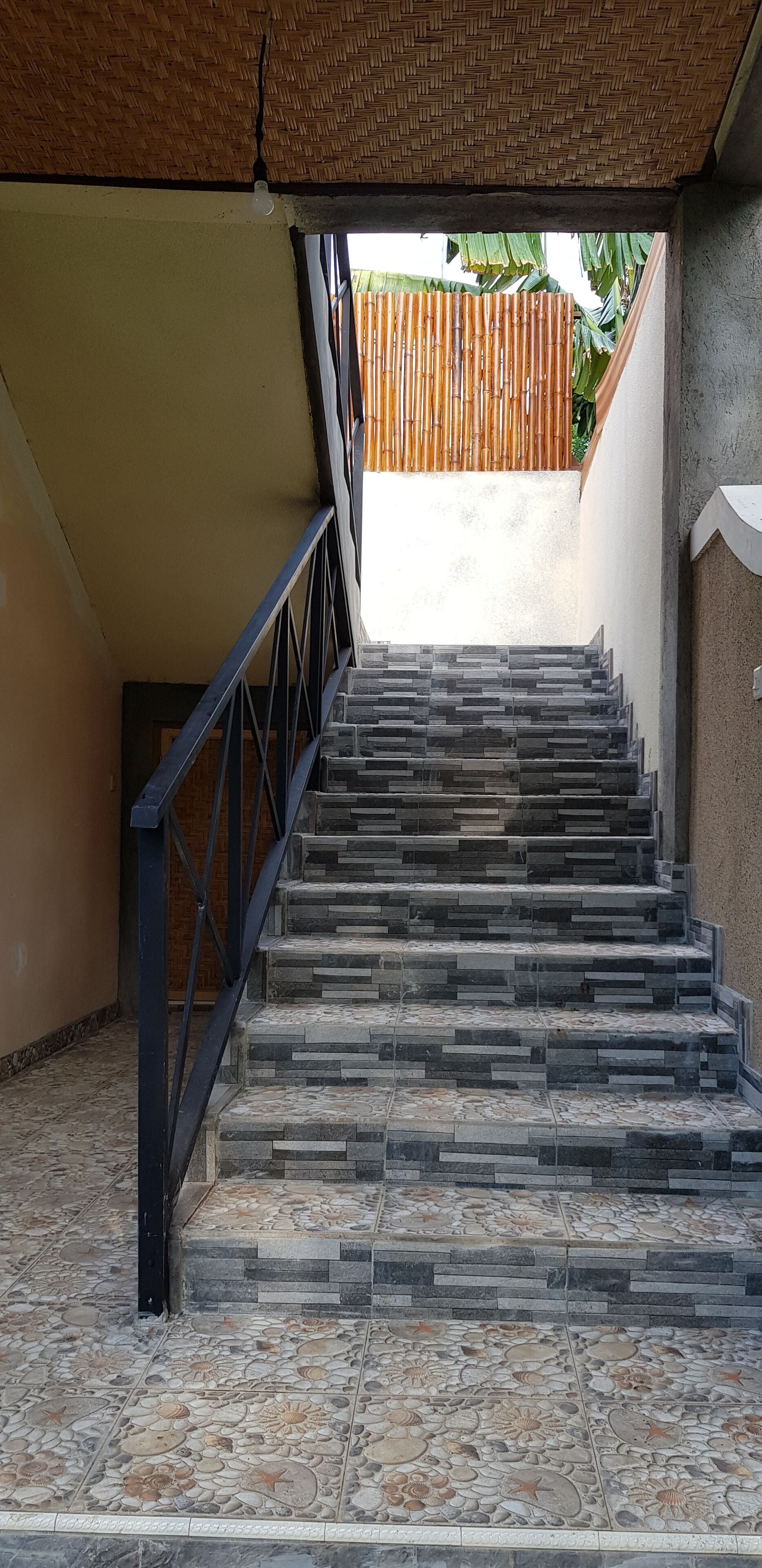 A staircase with a patterned tile floor leading to a covered area with a bamboo ceiling.