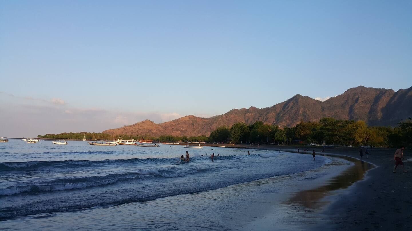 A beach with waves, boats, and mountains in the background.