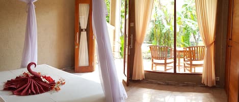 Un dormitorio con cama, dosel, balcón con sillas y vista a zonas verdes.