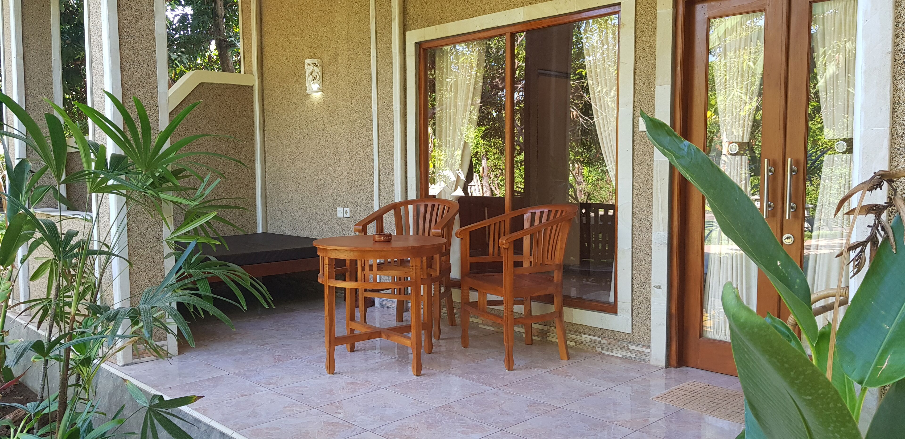 Un espacio de estar al aire libre cubierto con una mesa y sillas, rodeado de plantas y un ventanal corredero que da a un jardín.
