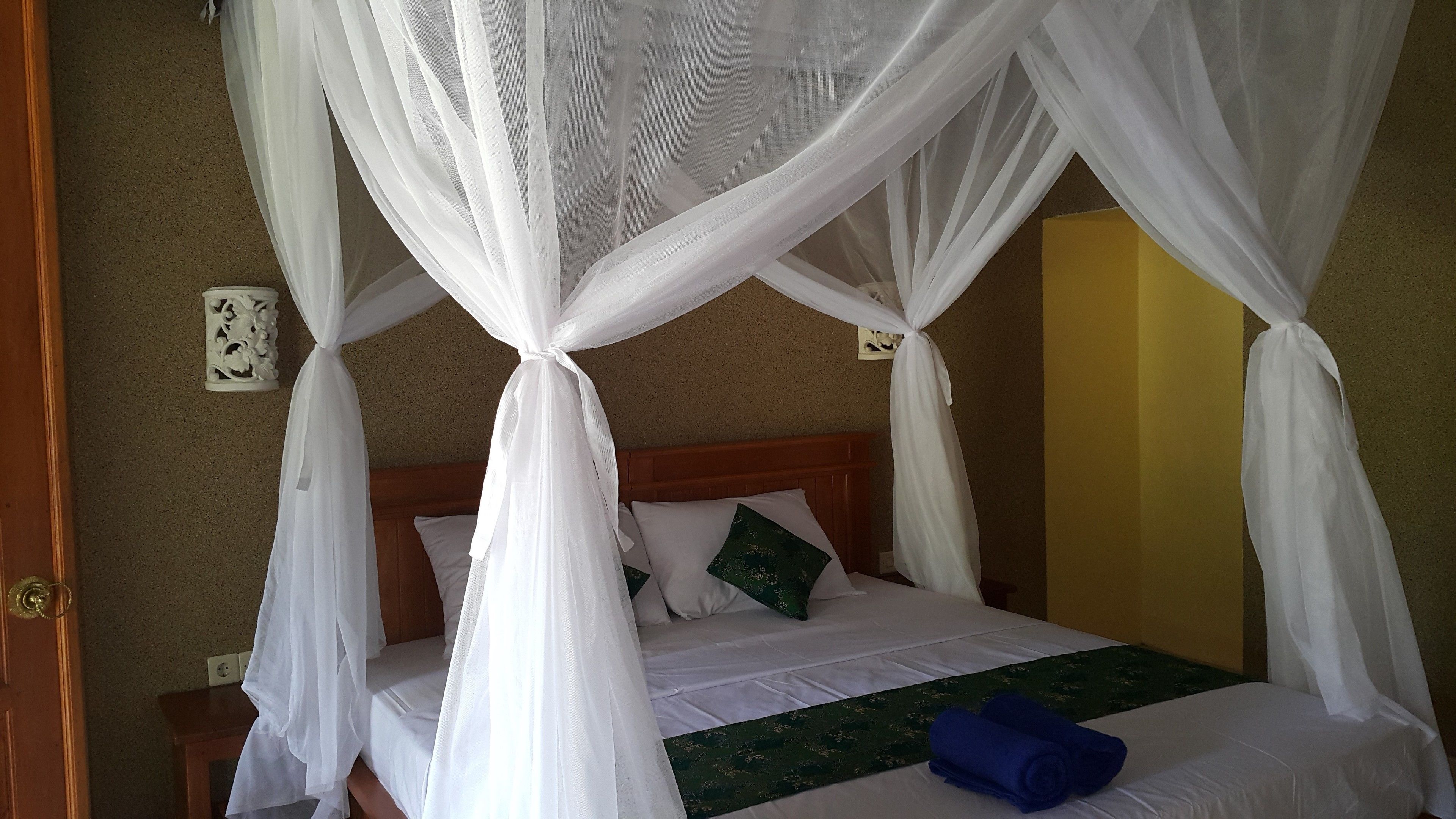 A bed with a canopy, a green bedspread, and a blue towel.