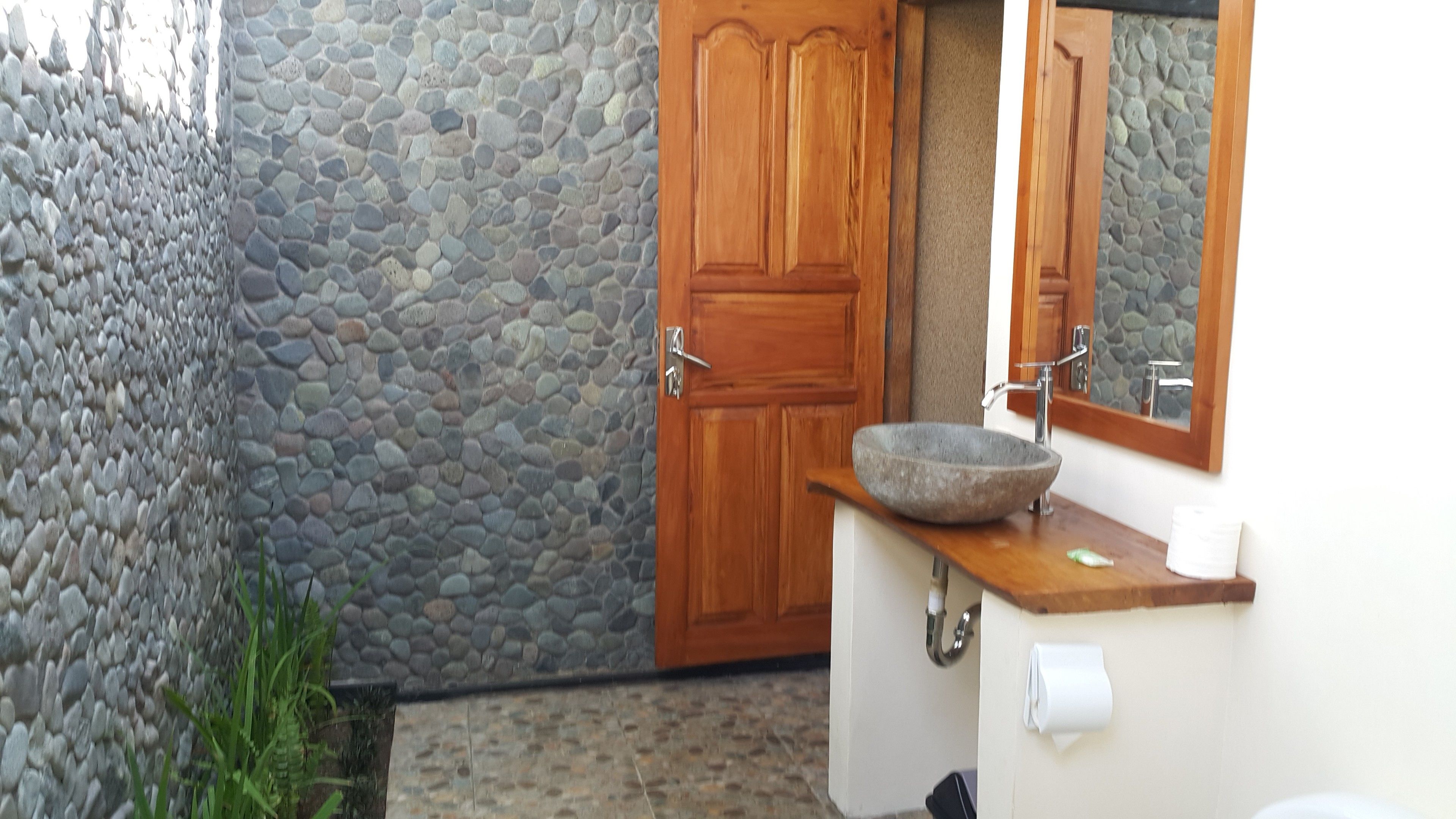 A bathroom with a stone wall, wooden door, and a stone sink.