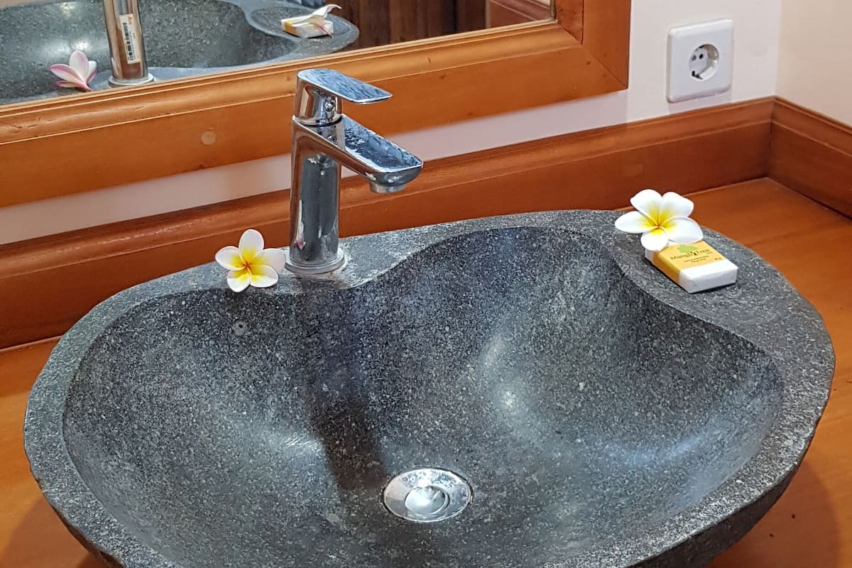 A stone sink with a modern faucet, a mirror reflecting a stone wall, and a wooden countertop.