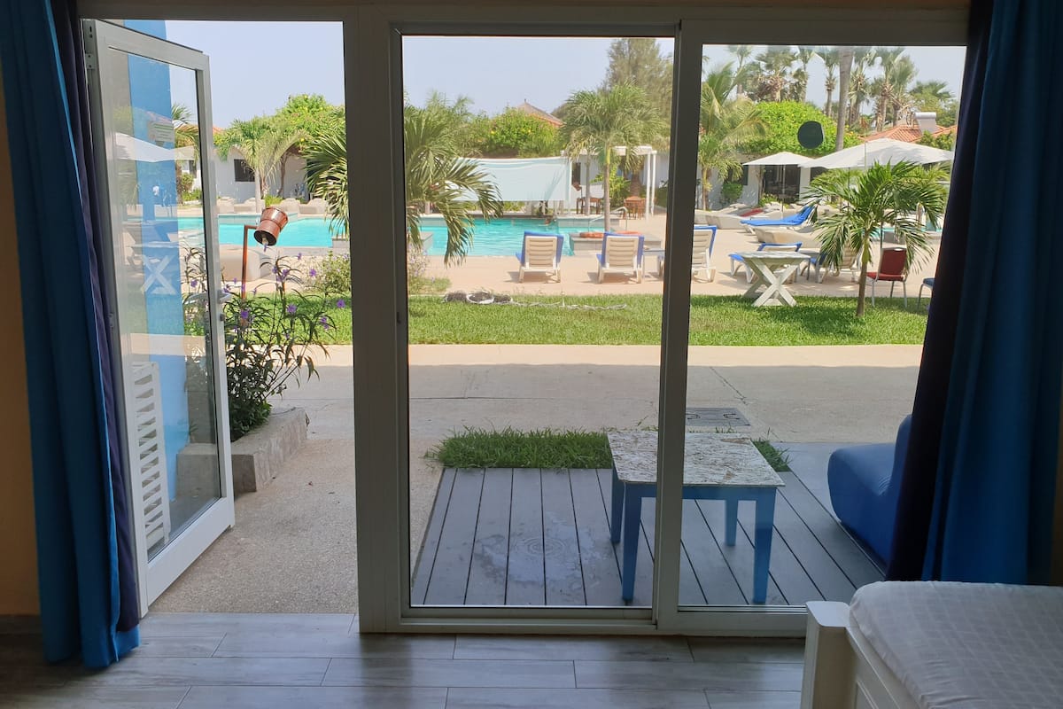 A room with a sliding glass door leading to a pool area with lounge chairs and a small table.