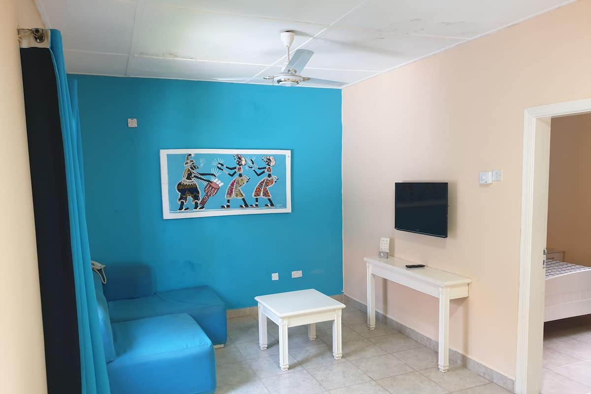 A room with a blue sofa, a white table, a TV, and a ceiling fan.