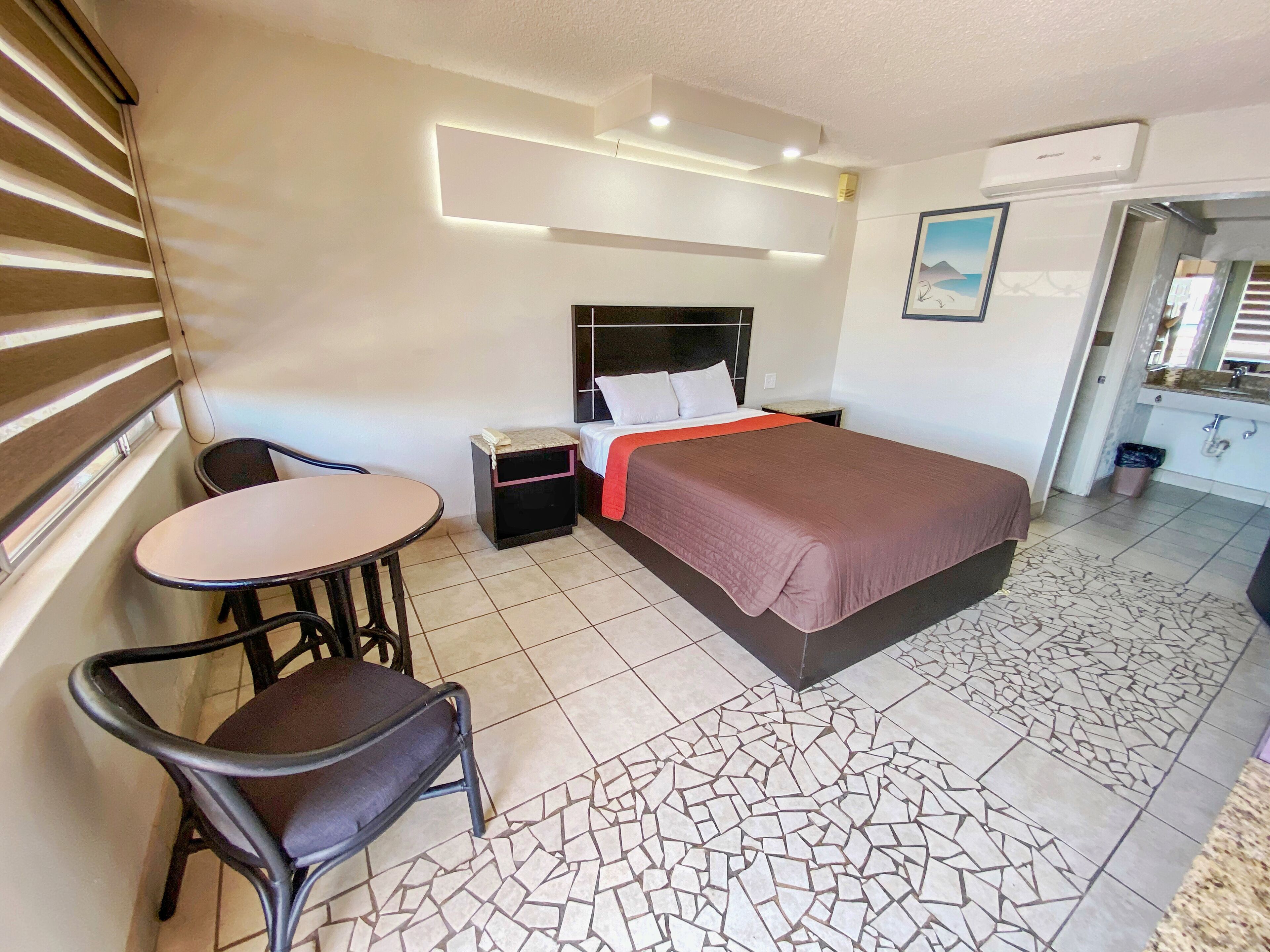 Habitación de hotel con una cama, una mesita de noche, una silla, una pequeña mesa y un baño visible a través de una puerta abierta.