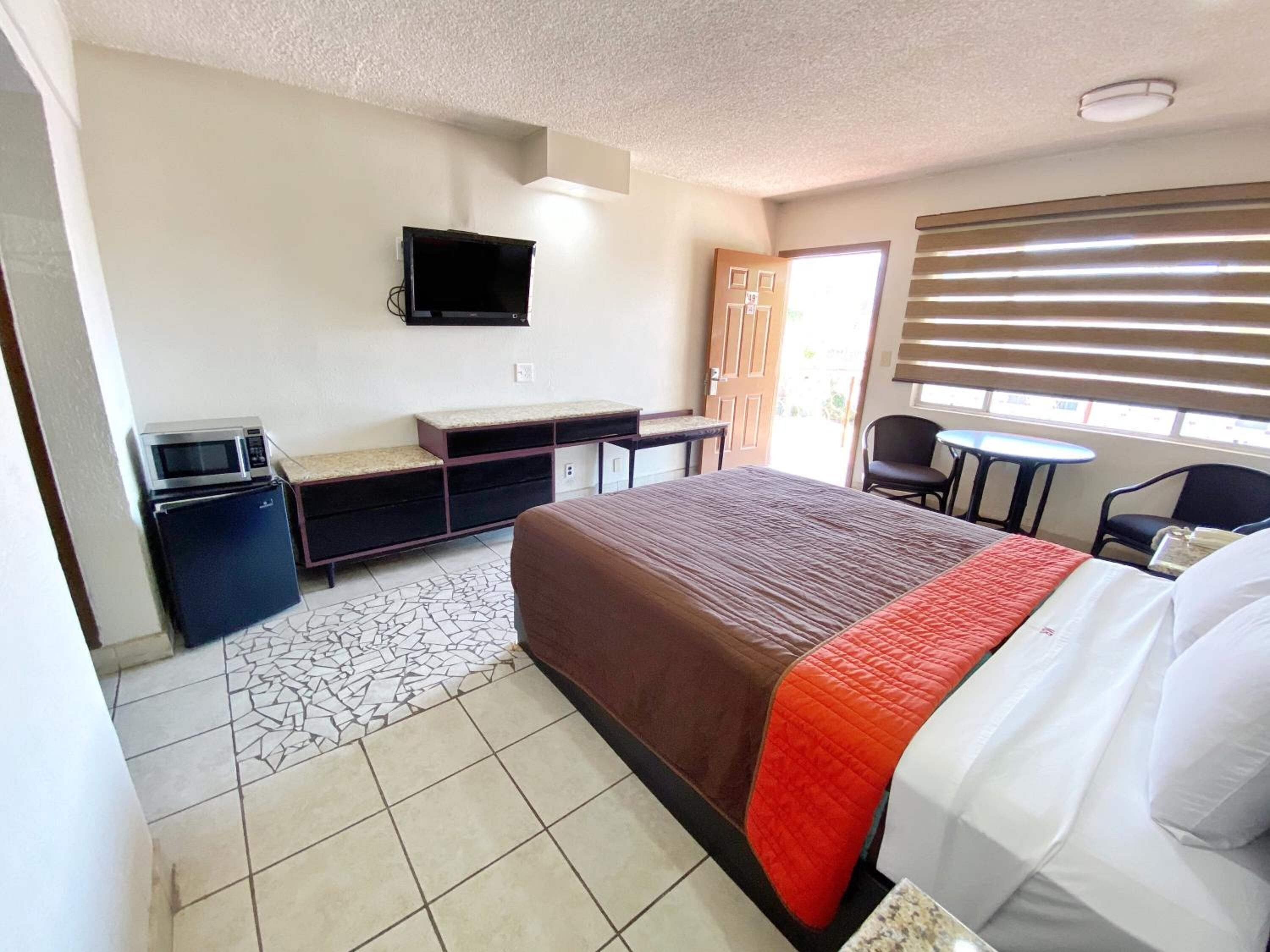 Habitación de hotel con una cama, un escritorio con computadora, televisión en la pared y una ventana con persianas.